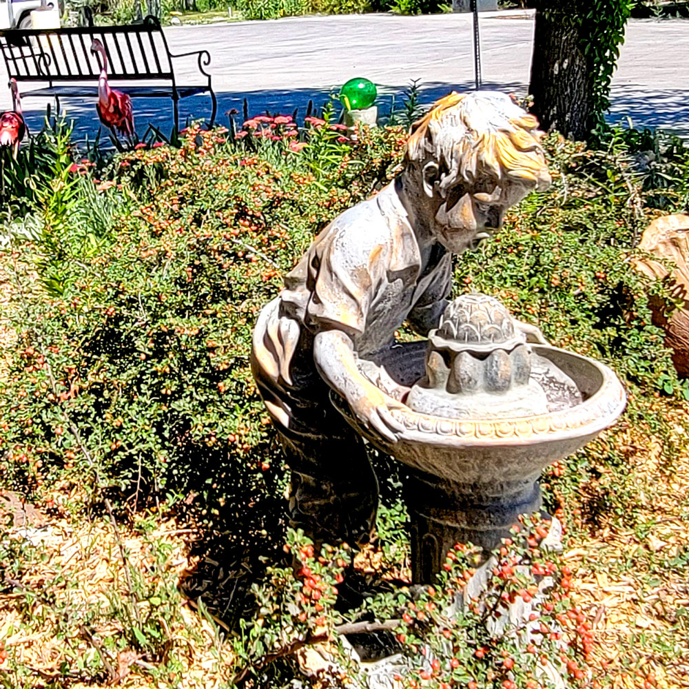 A statue of a boy who drinks water at a fountain in the retirement home garden.